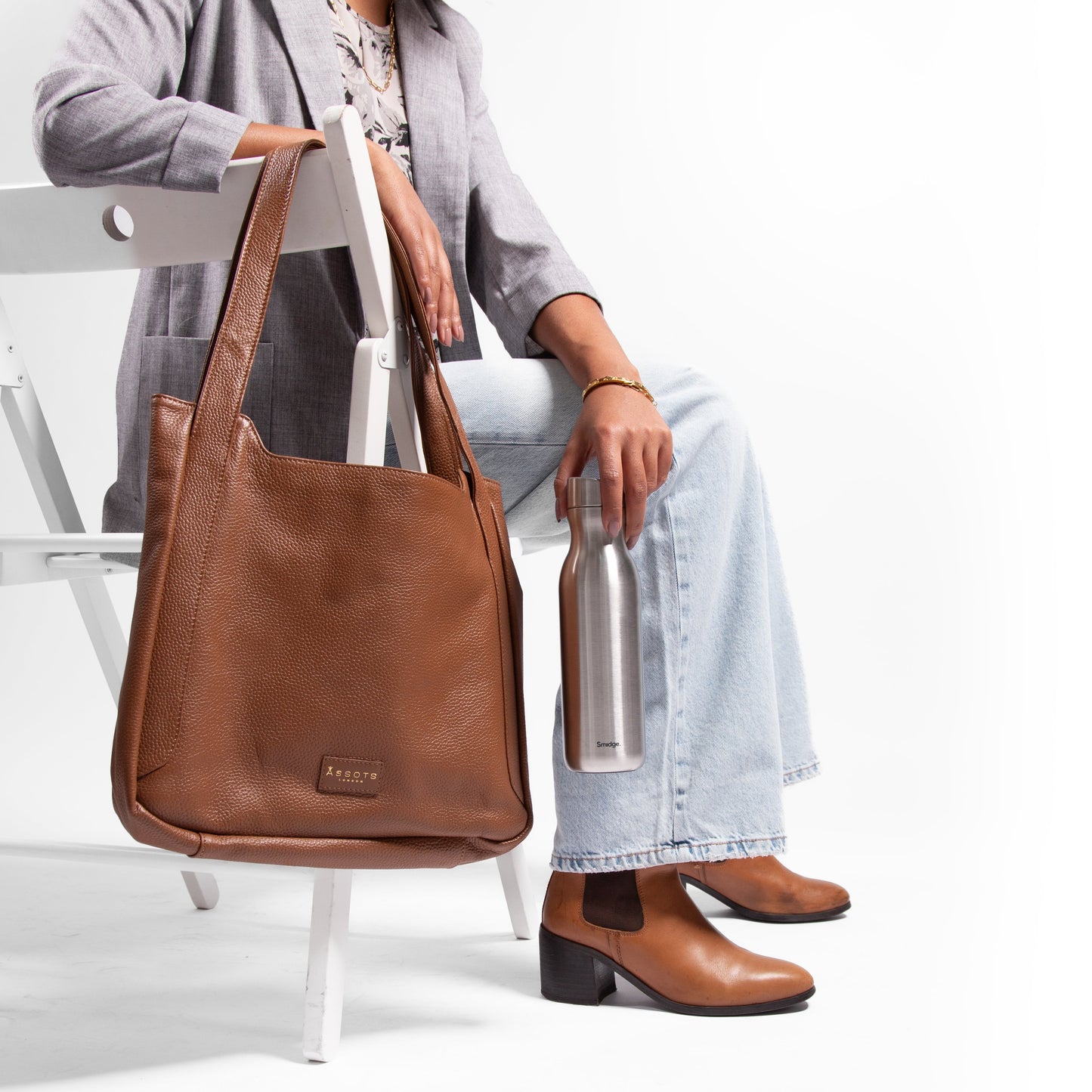 Woman sitting with a brown leather laptop handbag and holding a silver stainless steel 500ml water bottle