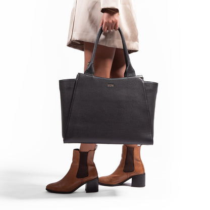 Woman holding a black, leather, laptop handbag with a white background