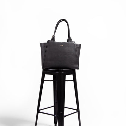 Black, leather, laptop handbag on a black metal stool against a white background