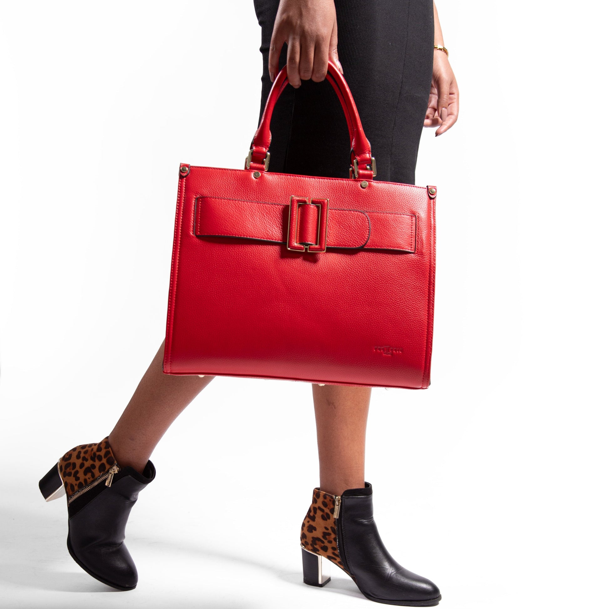 Red, leather, laptop handbag held by a person wearing black shoes with leopard print accents on a white background